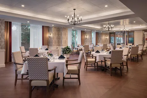 Dining room with set tables, upholstered chairs and chandeliers.