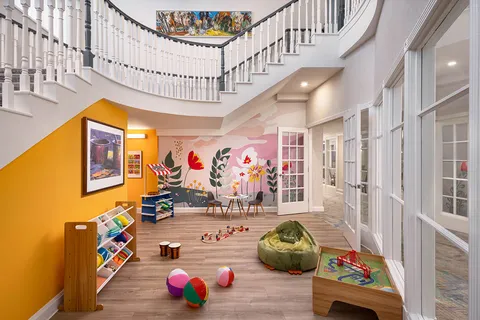 Playroom with toys, a mural and a staircase above.