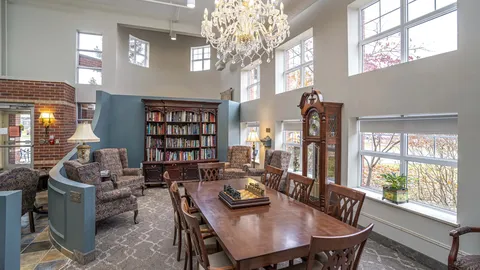 Table with a chessboard, armchairs, bookshelves and a chandelier