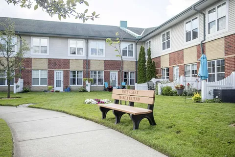 Residence building facing a lawn, paved path and wooden bench