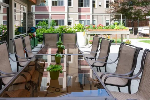 Patio with a long glass table, chairs and flower pots beside the building