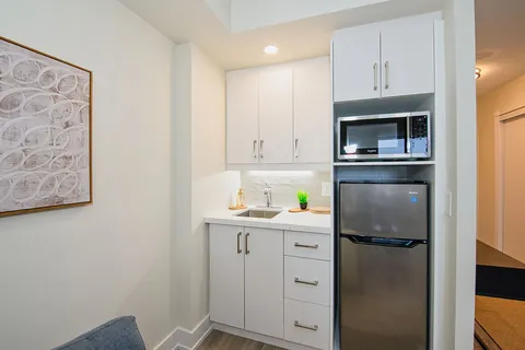White kitchenette with a sink, refrigerator and microwave.