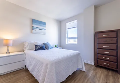 Bedroom with white bedding, a dresser and a small window
