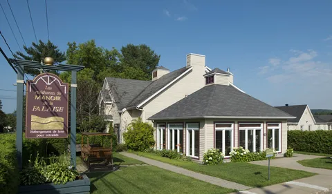 Cream residence with broad windows, flowerbeds, a lawn and a wooden garden swing