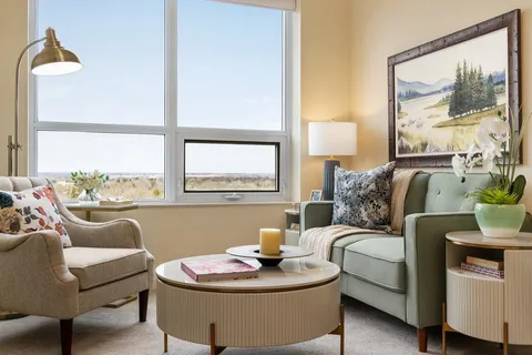 Living area with an armchair, sofa, coffee table and large window.