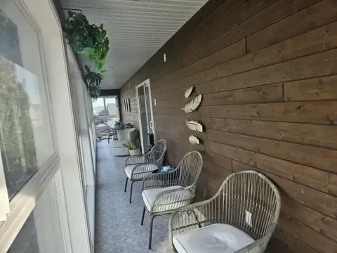 Covered patio with wicker chairs, small tables and a wooden wall