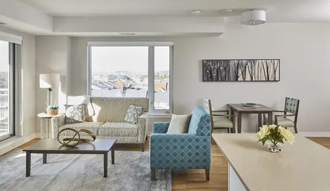 Sitting and dining area with a sofa, blue armchair and table beside a window