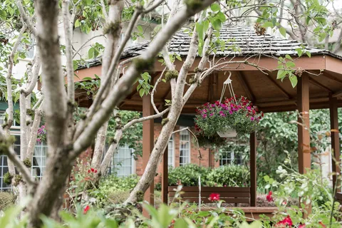 Garden with a gazebo, mature trees and flowering plants.