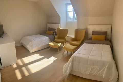 Shared bedroom with two beds, chairs and a window.