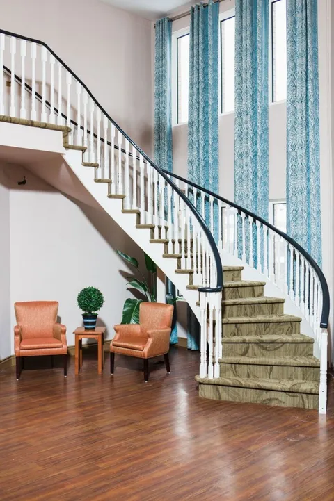 Curved staircase beside tall windows and two orange armchairs