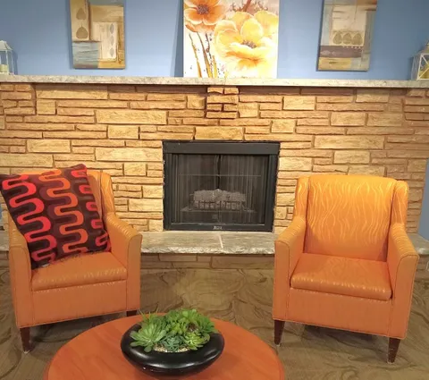 Two orange armchairs beside a stone fireplace and floral artwork