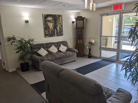 Entrance lobby with grey sofas, a grandfather clock, plants and glass doors.