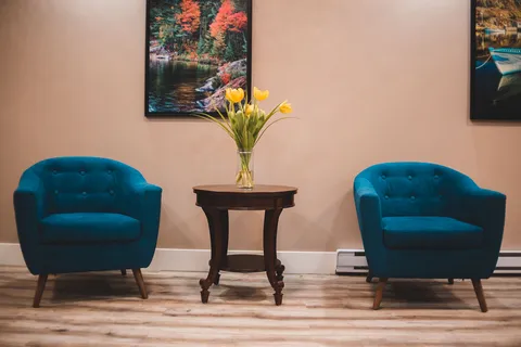 Two blue armchairs beside a small table and wall art.