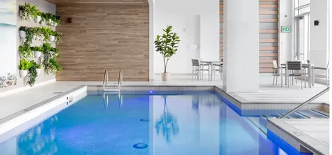 Indoor swimming pool with a tiled surround, plants and tall windows