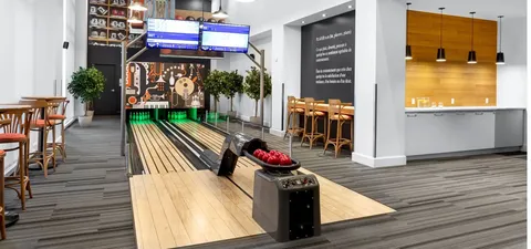Two bowling lanes with score screens, seating and a guitar mural
