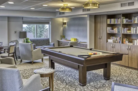 Billiards table beside lounge chairs and library shelving.