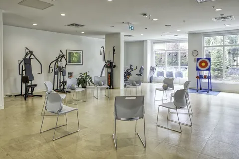 Exercise room with chairs, strength equipment and large windows.