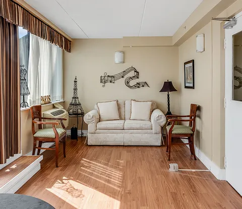 Room with a cream sofa, wooden armchairs, musical-note wall decor and tall windows