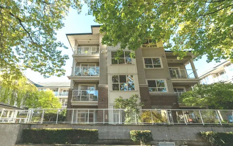 Multi-storey building with balconies and trees beside a glass greenhouse