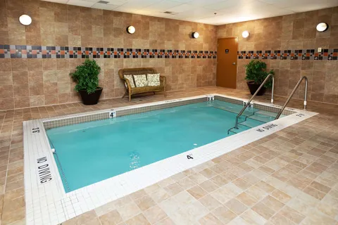 Indoor pool with tiled walls, metal steps, plants and a bench