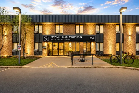 Front exterior with a covered entrance, access ramp and lights at dusk.