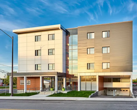 Four-storey building with beige and grey siding, a glass stairwell and a ground-level entrance