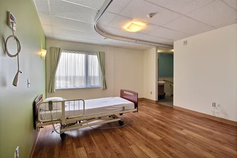 Bedroom with an adjustable bed, ceiling lift, green curtains and an open bathroom doorway