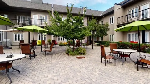 Brick courtyard with tables, green umbrellas and a central tree.