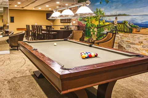 Billiards table beneath pendant lights beside a wall mural.
