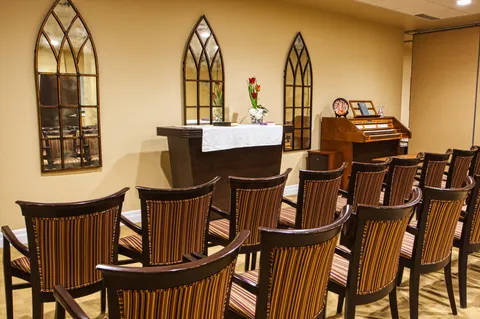 Chapel seating facing an altar and upright piano.