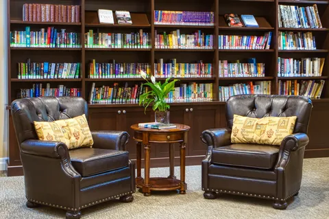 Library shelves behind leather armchairs and a small table.