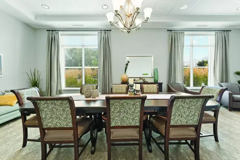 Dining table and chairs beneath a chandelier beside two windows