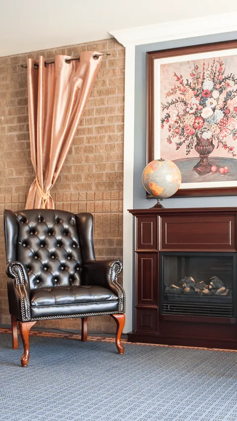 Tufted leather armchair beside a fireplace with a globe and framed floral artwork