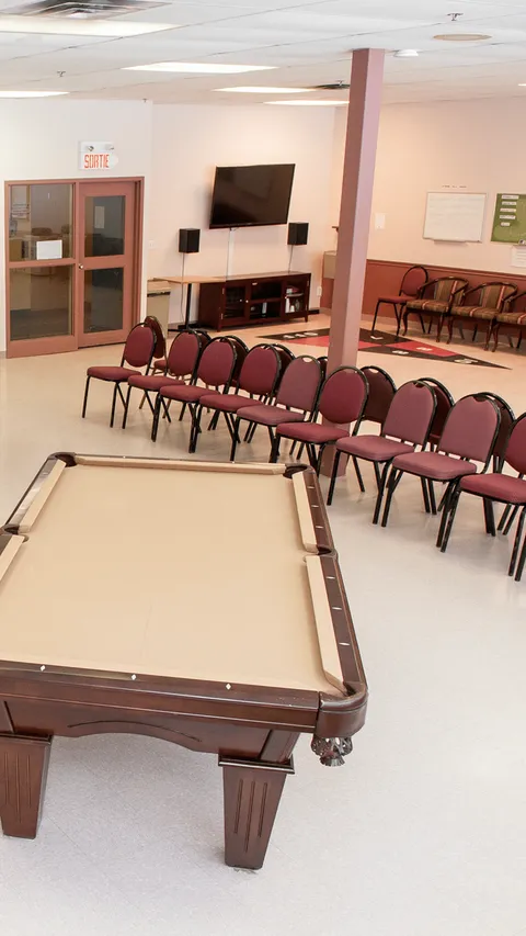 Activity room with a pool table, rows of burgundy chairs and a wall-mounted television