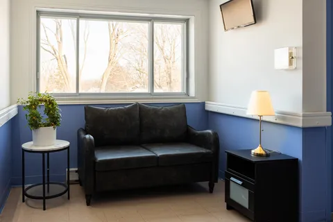 Black sofa beside a large window, a potted plant and a table lamp