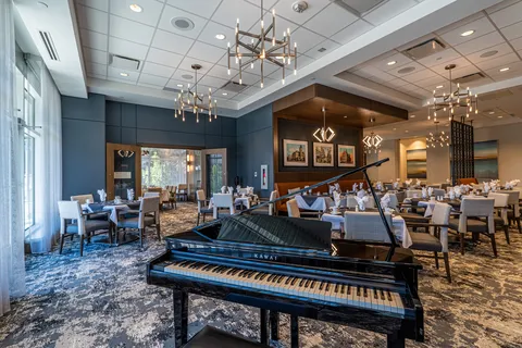 Dining room with tables, chairs and a grand piano.