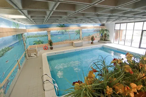 Indoor swimming pool with chairs along its sides.