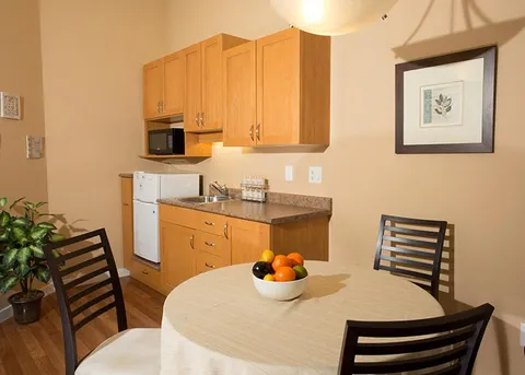 Suite kitchenette with wooden cabinets beside a dining table.