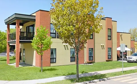 Two-storey residence with brick columns, balconies, trees and a lawn.