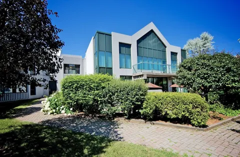Residence building behind shrubs and a paved path.