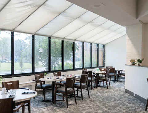 Dining tables and chairs beneath a sloping glass roof beside tall windows