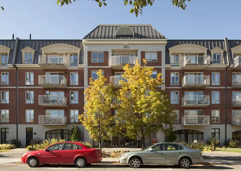 Front facade of a brick building with balconies, trees and cars along the street