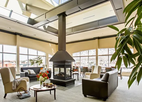 Armchairs and tables around a suspended fireplace beneath large windows