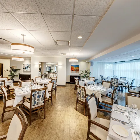 Dining room with white tablecloths, set tables, patterned chairs and wall paintings