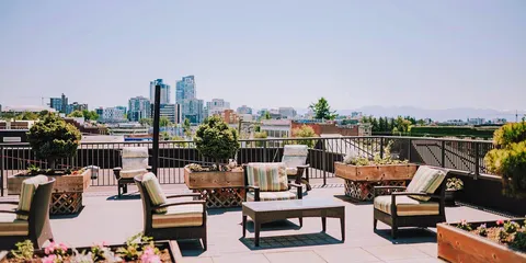 Rooftop terrace with cushioned chairs, wooden planters and a view of city buildings