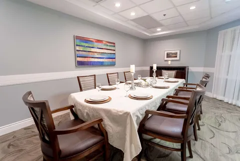 Dining table set with plates, napkins and glassware beside an abstract painting
