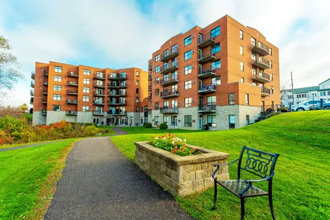 Brick residence with balconies above a lawn, walking path and flower bed