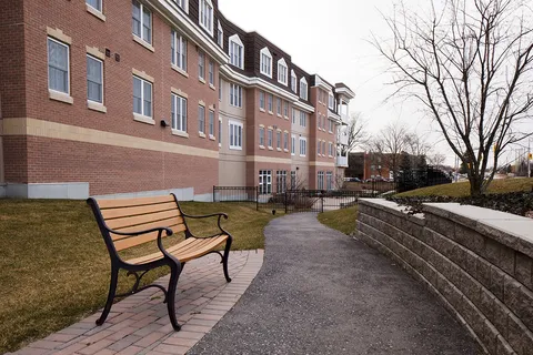 Residence building beside a walking path, bench and lawn.