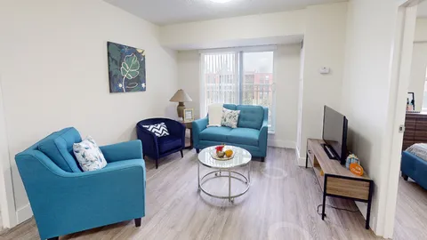 Suite living room with blue armchairs, a television and round coffee table.