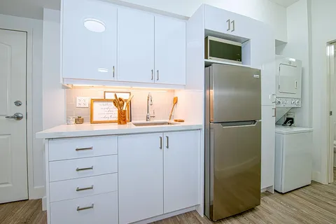 Kitchenette with white cabinets, sink and refrigerator.